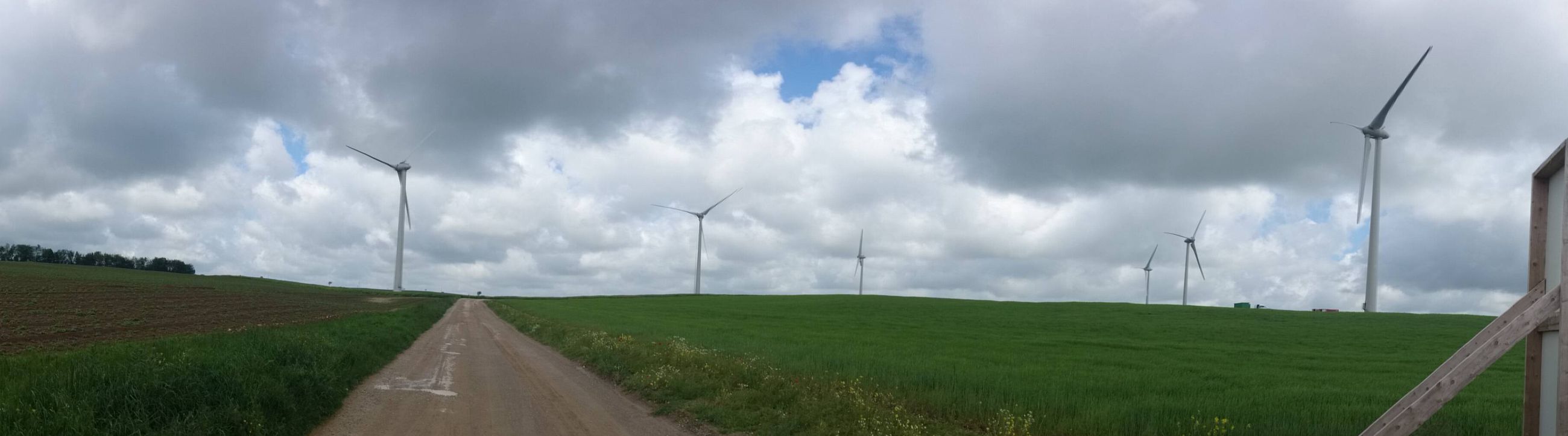 Ligne d'éoliennes au-dessus de champs sous un ciel nuageux